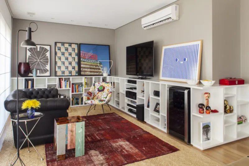 Para acomodar livros, objetos, equipamentos e eletrodomésticos em uma sala pequena, em que não havia muita distância entre o sofá e a parede oposta, Arruda criou uma estante em MDF laqueado branco de meia parede. “A ideia foi aproveitar espaço não para cima, mas para os lados”, diz. Foto: Victor Affaro/Divulgação