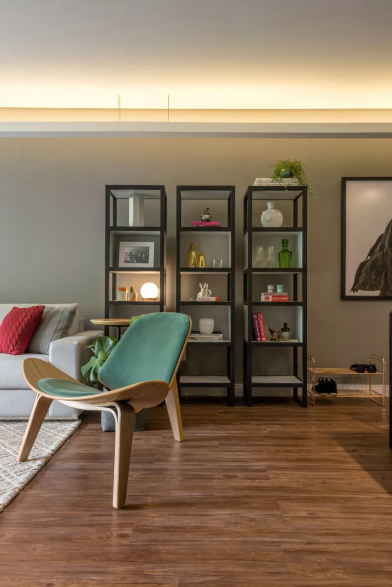 Composta por três unidades iguais, a estante em MDF e melamínico criada por Ana Carolina e Corsi atua como um elemento vertical em uma sala integrada com predominância de linhas horizontais. Espaços com e sem fundo criam um jogo de relevância no móvel: dependendo da cor do objeto, ganha mais destaque em um nicho ou em outro. A luminária cria efeitos nas prateleiras e na parede. Foto: Fernando Zequinão/Gazeta do Povo