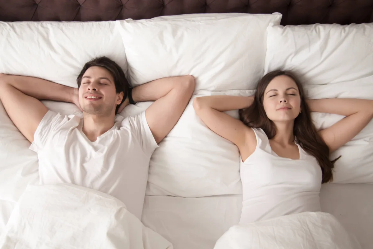 Casal deitado lado a lado, feliz após uma noite de sono reparadora.
