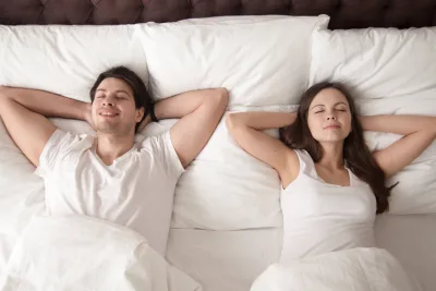 Casal deitado lado a lado, feliz após uma noite de sono reparadora.