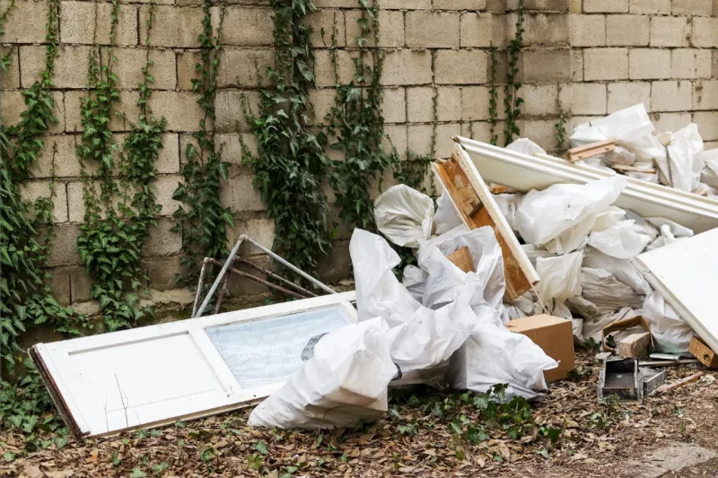 Construction garbage after apartment repair. Pile of construction waste near a white brick wall. Construction debris in white bags prepared for disposal in a landfill.