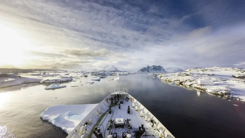 A ship crusing among icebergs between frozen land of Antarctica and islands surrounding it