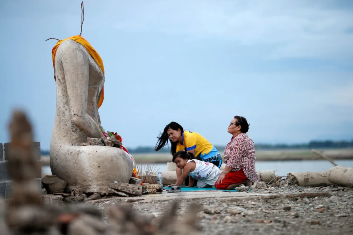 Família reza perto das ruínas de uma estátua de Buda que ressurgiu após seca baixar nível de barragem em Lopburi, na Índia. Foto: G1/Reprodução/Soe Zeya Tun/ Reuters
