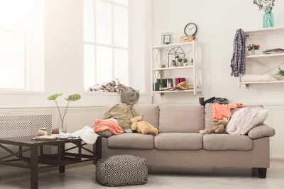 Sofa in messy living room with many stack of clothes. Disorder and mess at home, copy space