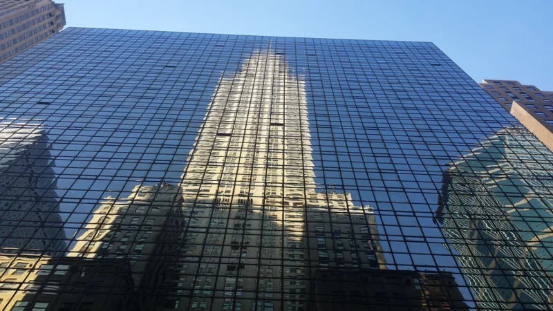 Foto: Chrysler Building refletido em arranha céu moderno.