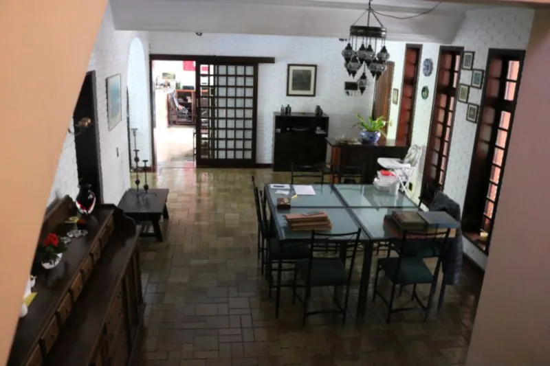 Nas salas, alguns dos destaques são as mesas de vidro, o jogo de mesa de jantar de Imbuia com dez cadeiras e dois aparadores, lustres e uma estante em módulos para montar conforme o espaço disponível.