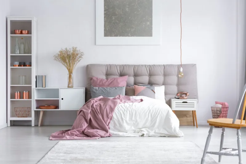 Spacious cozy master bedroom interior with copper decorations on the white rack wooden chair and buttoned gray headboard