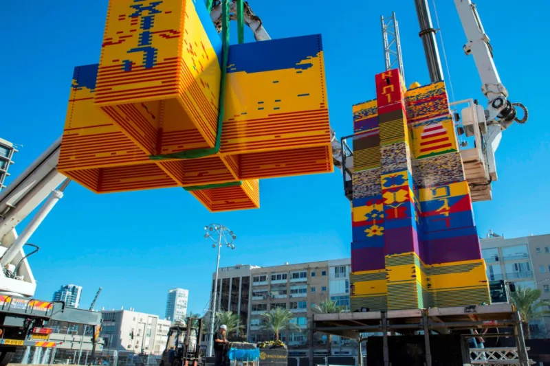 Workers and volunteers help assemble bricks during the construction of a LEGO tower in Tel Aviv's Rabin Square on December 26, 2017, as the city attempts to break Guinness world record of the highest such structure. / AFP PHOTO / JACK GUEZ