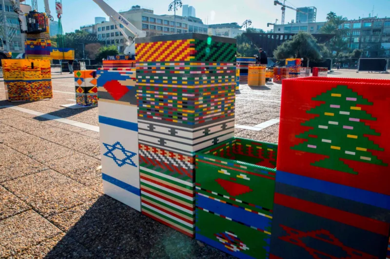 Workers and volunteers help assemble bricks during the construction of a LEGO tower in Tel Aviv's Rabin Square on December 26, 2017, as the city attempts to break Guinness world record of the highest such structure. / AFP PHOTO / JACK GUEZ