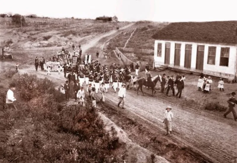 Préstito desfilando ao som da banda militar pela antiga Estrada do Portão, hoje Avenida República Argentina, a fim de participarem da inauguração da Sociedade Internacional da Água Verde no dia 1.º de janeiro de 1905. Ao fundo, o espaço da atual Praça do Japão. Foto: Reprodução/Gazeta do Povo