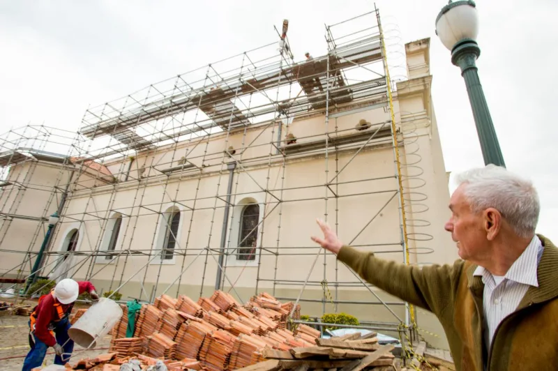 O padre Claudio Ambrozio, pároco da igreja, mostra os detalhes da obra na parte externa do prédio. A ideia de restaurar a igreja veio depois que pedacinhos de cimento caíram sobre ele durante uma missa. Foto: Hugo Harada/Gazeta do Povo