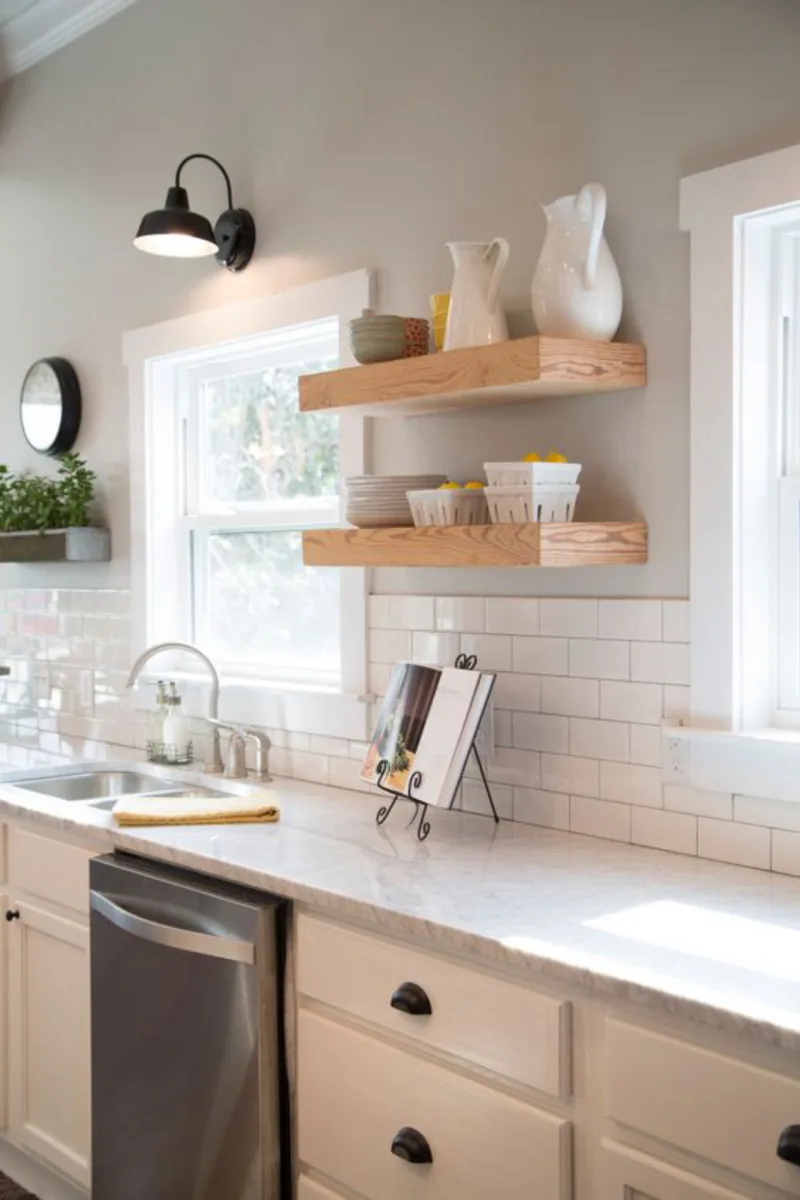 Fixer Upper Hosts Chip and Joanna Gaines have gutted and transformed the kitchen. They added new Carrera marble countertops, cabinets, floating wood shelves, a subway tile backsplash, and fresh light gray paint. Stainless appliances and a stainless sink and faucet are clean and modern, as seen on HGTV's Fixer Upper. (After 11a) Afters