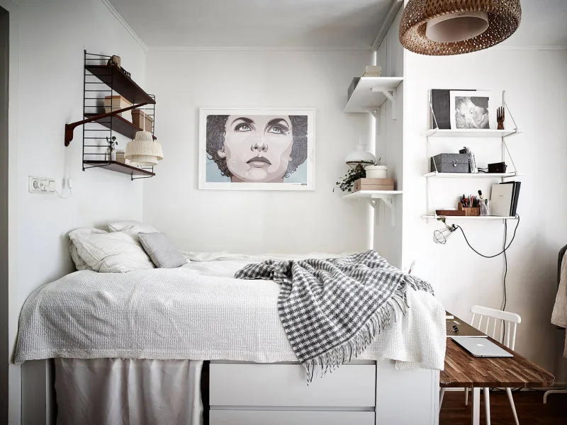 Prateleiras com materiais diversos são o principal artifício usado para organizar e ao mesmo decorar o apartamento. Aos pés da cama há espaço até para um charmoso home office.