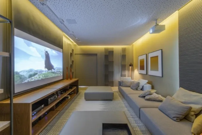 Neste projeto de Patrícia Penna Arquitetura & Design de Interiores, a iluminação lateral no teto torna a luz indireta no cômodo e não interfere refletindo na tela do televisor