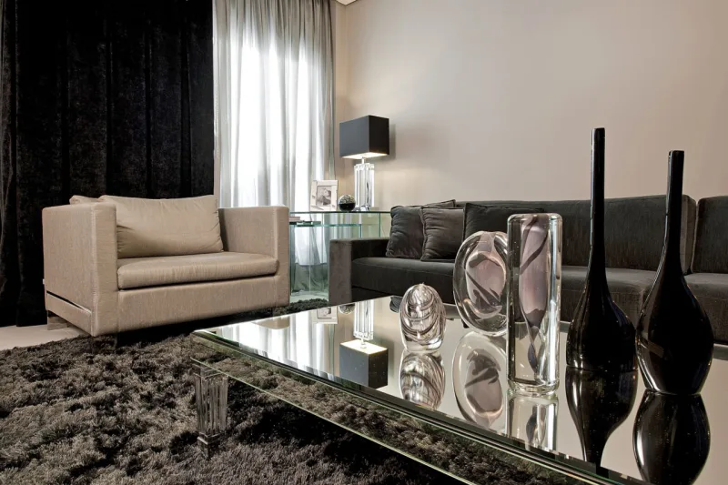 Outra sala da residência com tapete e sofá pretos. O que quebra a sequência mais escura é a poltrona bege.