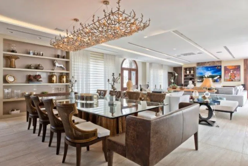 Sala de jantar com destaque para o lustre de cristais e bronze, que ocupa toda a mesa. Os quadros da sala são assinados por Luis de Souza.