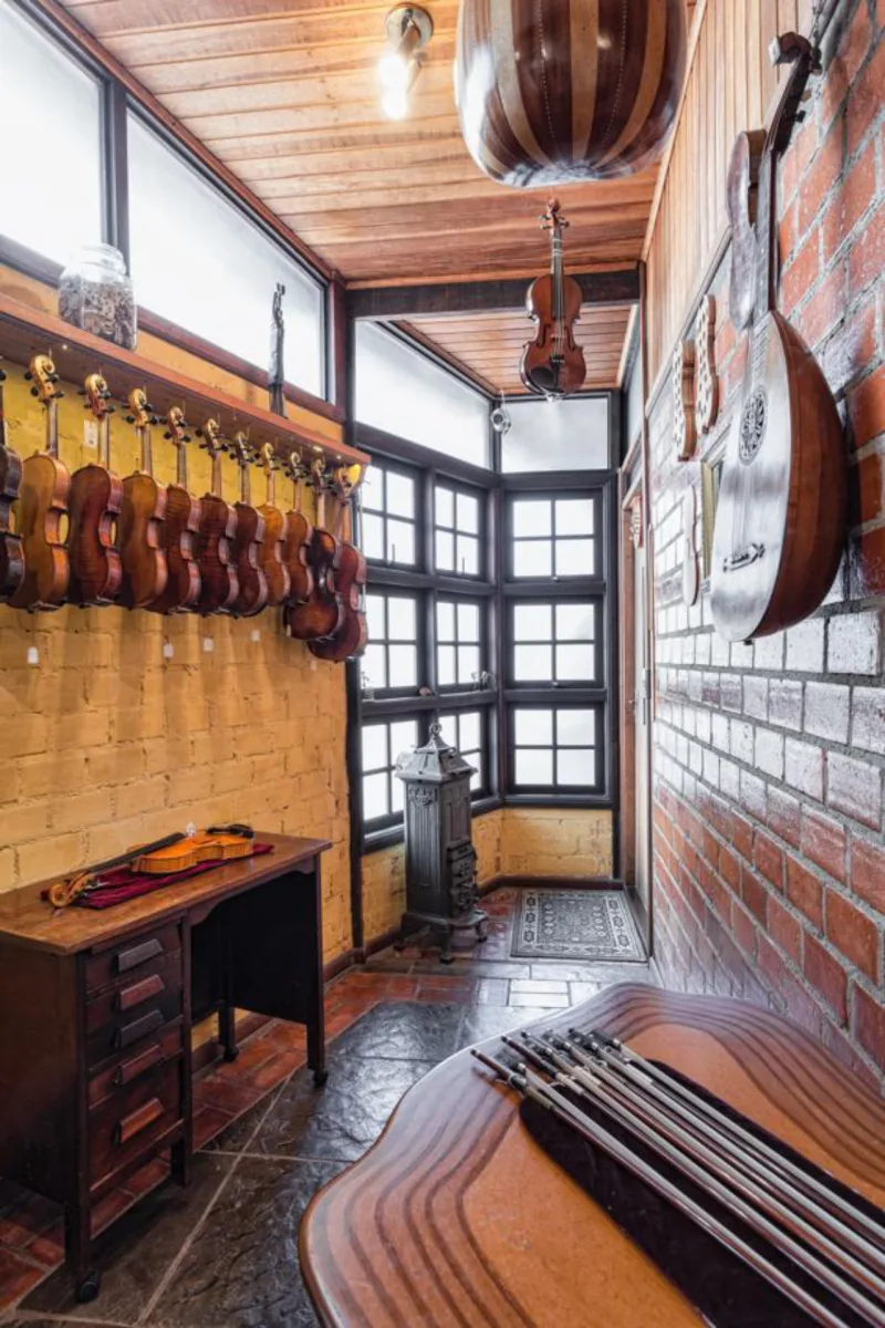 Cozinha da casa dos Amorim tem portas de janelas de demolição e um fogão a lenha antigo. Acima, parede com os violinos construídos por Luiz e a parede com pintura de cal. Foto: Fernando Zequinão/Gazeta do Povo