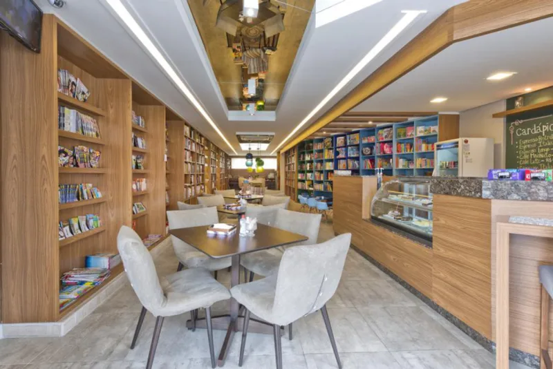 Um antigo restaurante deu lugar a uma livraria com perfil retrô, em São José dos Pinhais. Cores e tecidos diferenciados, como o jeans manchado e tons de listrado, dão o tom vintage da ambientação, que traz peças de design, como a mesa em forma de caixa de fósforo, do designer paranaense Gustavo Eugelhardt, e caixas de madeira reaproveitadas para guardar livros. Painéis amadeirados e mobiliário com cores sóbrias contrastam com peças de tons vibrantes, como os pendentes em degrade de azul e verde. O projeto de iluminação, com rasgos de luz no gesso e fitas de LED, dá um toque sofisticadinho e acolhedor. Foto: Divulgação