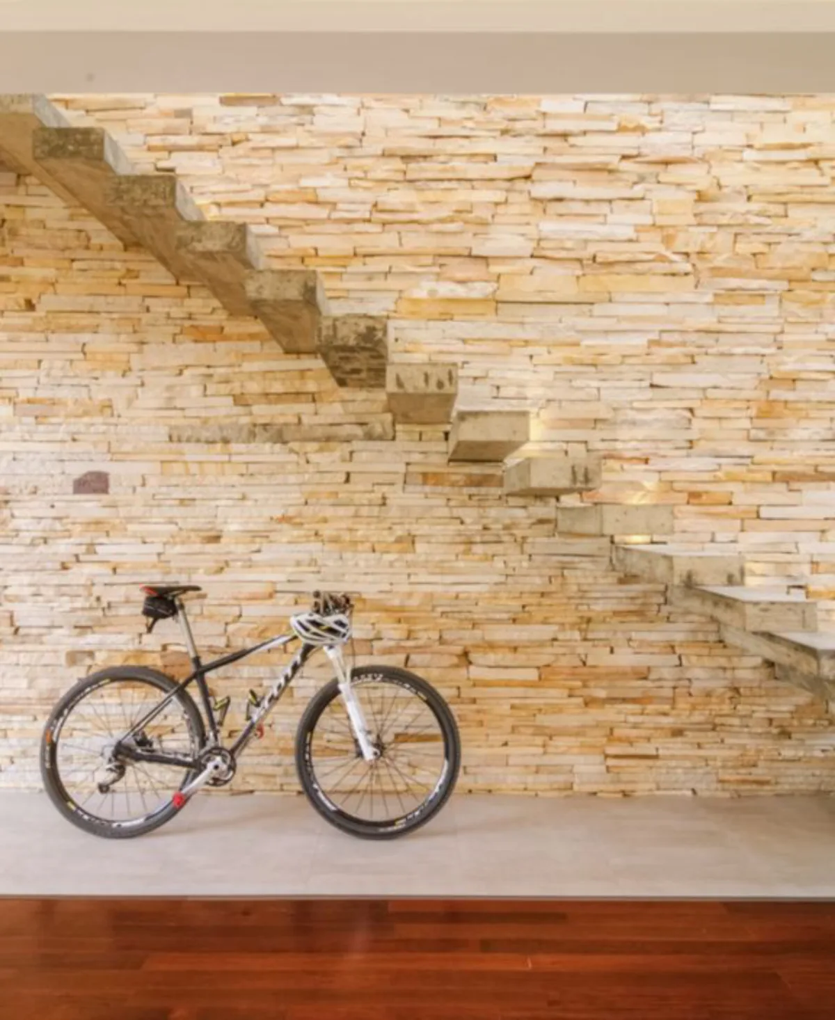 Ponto Focal: “A escada deve ser um show à parte.” Esse foi o pedido do jovem casal, que ama natureza, esportes (dá para ver pela bike como elemento de destaque) e receber os amigos. Enquanto os filhos não vêm, a escada fica sem corrimão, mas o guarda-corpo de vidro temperado já foi planejado pela arquiteta Leticia Kunow, para ser fixado nas laterais dos degraus de concreto armado moldado in loco. Eles compõem com parede revestida com pedra arenito rústico, piso em madeira escura e cerâmica clara