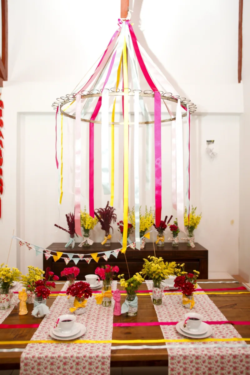 Mesa de apoio: Providencie uma mesa para que os convidados sentem e nela coloque as mesmas toalhas e potes de compotas, adornados com retalhos de tecido, como vasos para flores coloridas. “A ideia é usar aquelas flores de jardim, como dálias e margaridas”, explica Tatiane. Quem não tiver um jardim em casa, pode comprar flores do campo, que são baratas e coloridas. Fazendo referência à dança das fitas, tradicional nas festar juninas, pode-se usar uma estrutura redonda presa ao teto, como um bambolê, por exemplo, e prender fitas de cetim de diversas cores. Foto: André Rodrigues / Gazeta do Povo