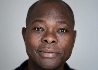 Plano fechado do arquiteto Diébédo Francis Kéré, um homem negro, careca, com olhos amendoados, nariz de base larga e lábios volumosos.