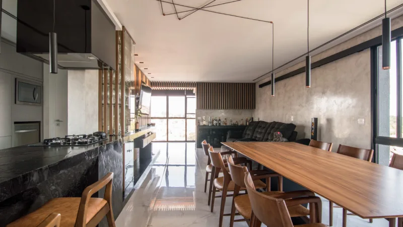 Uma ampla sala integrada é o principal cômodo da casa. O mobiliário é majoritariamente em madeira, que também está presente nas ripas na cozinha, churrasqueira e bar.